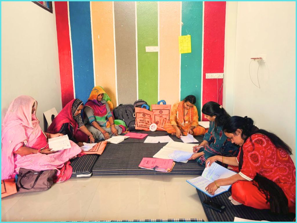 A group of women sitting on the floor in a brightly colored room, engaged in discussions and reviewing documents.