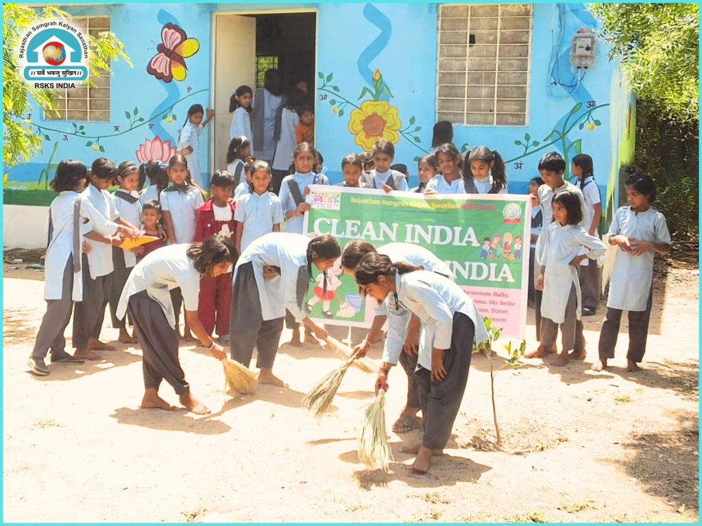 Group of children participating in a cleanliness drive, sweeping the ground in front of a colorful building.