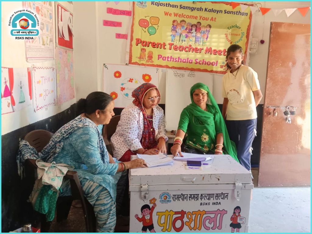 A parent-teacher meeting at Pathshala School, featuring four women sitting and standing near a table with educational materials, surrounded by colorful posters on the walls.