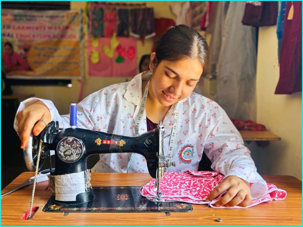 A young woman sewing a patterned fabric on a vintage sewing machine in a workshop setting, displaying a focused expression and wearing a floral print shirt.