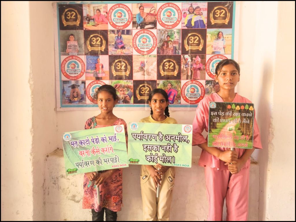 Three children holding signs promoting environmental awareness in front of a collage of photographs, celebrating the 32nd anniversary of RSKS India.