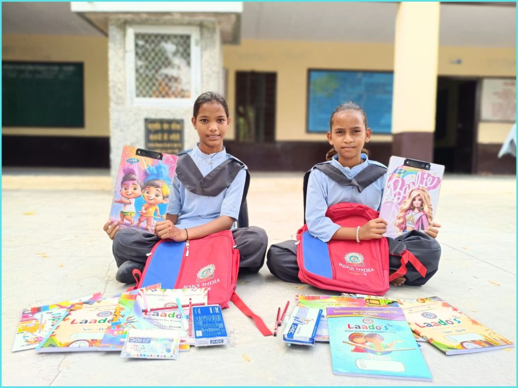Two schoolgirls sitting on the ground, each holding a colorful book, surrounded by school supplies and backpacks.